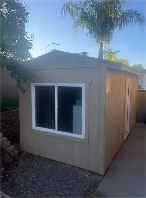 Custom-built storage shed with a locking door and sliding window, on a gravel pad.