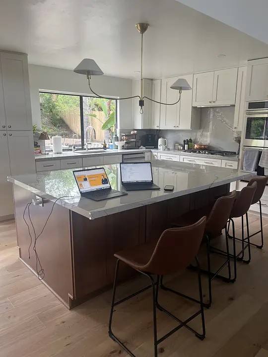 Finished kitchen in daily use: large island with bar stools, garden window, laptops left on the counter.