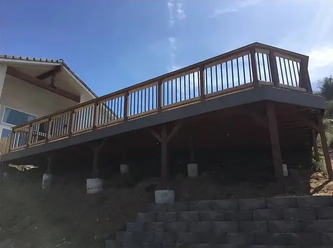 Elevated wooden deck attached to a house, posts and framing visible over a block retaining wall. Photographed mid-build.
