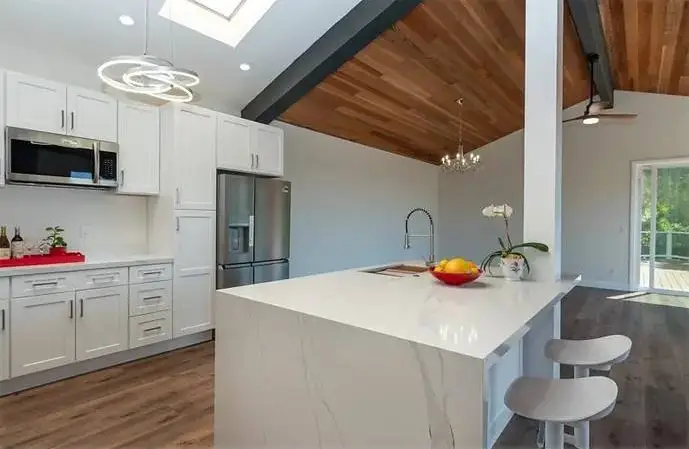Kitchen with a marble-topped island, wood ceiling, bar stools and a stainless fridge.