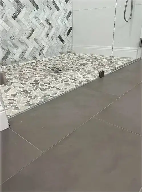 Walk-in shower: herringbone wall tile, pebble mosaic floor, frameless glass and a large-format porcelain floor.
