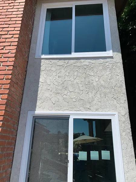 Two white-framed windows installed in a stucco-and-brick elevation.