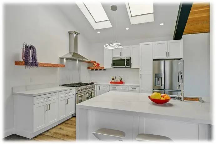 Kitchen with white cabinets, skylights in a vaulted ceiling, stainless appliances and a waterfall island.
